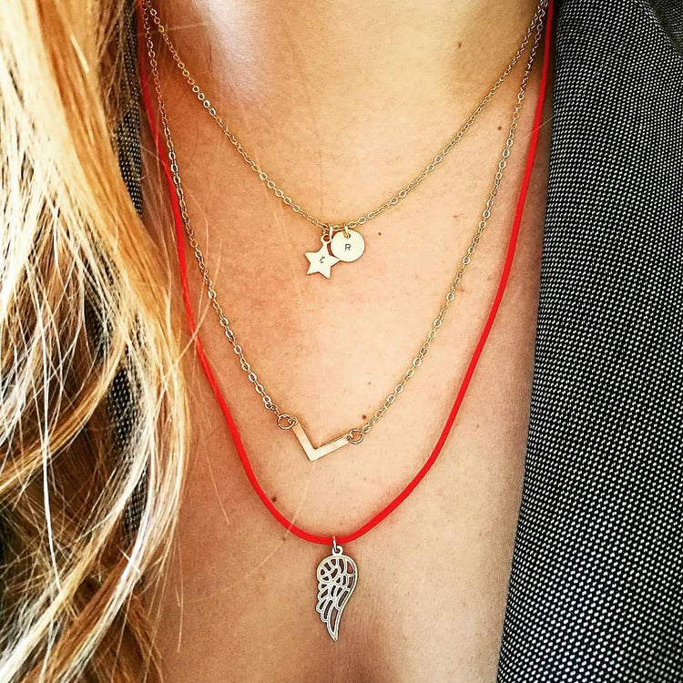 Gelaagde gouden initial necklace set met gegraveerde ster en letterbedel, gecombineerd met een chevron ketting en engelenvleugel sieraad van lux & luz.