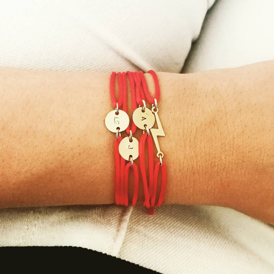 Een eclectische stack van 14k gold filled satijnen armbandjes op de pols van een vrouw; toont de bliksem armband gecombineerd met een 'Initiaal S' cord bracelet en de 'Boho Pijl'. Een symbool voor persoonlijke energie en focus. Waterproof en biocompatibel.