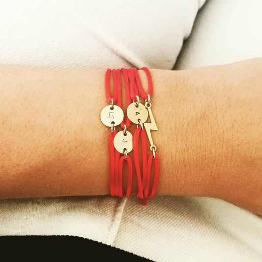 Een eclectische stack van 14k gold filled satijnen armbandjes op de pols van een vrouw; toont de bliksem armband gecombineerd met een 'Initiaal S' cord bracelet en de 'Boho Pijl'. Een symbool voor persoonlijke energie en focus. Waterproof en biocompatibel.