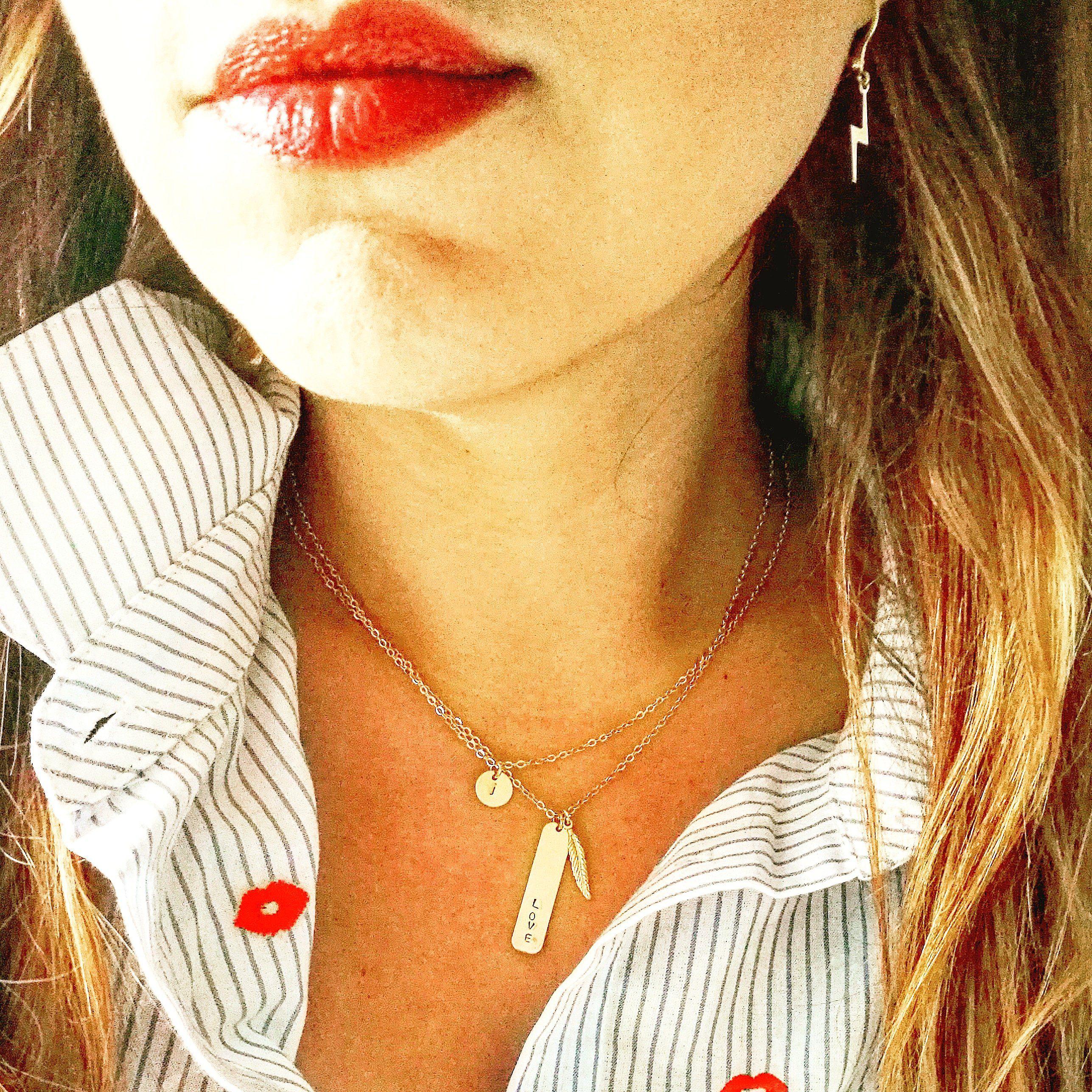 Vrouw draagt de goud gevulde veer ketting uit de Boho & Elements collectie, gecombineerd met andere minimalistische hangers.