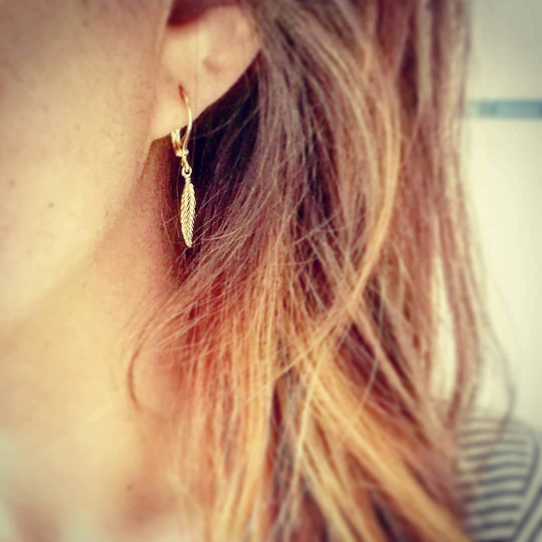 Gedetailleerde opname van de gouden veer oorbellen, 24/7 jewelry van Nederlands atelier-kwaliteit die nooit verkleurt.