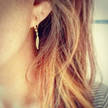 Gedetailleerde opname van de gouden veer oorbellen, 24/7 jewelry van Nederlands atelier-kwaliteit die nooit verkleurt.